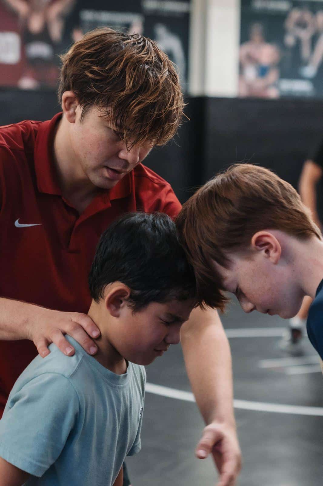 Coach Jaden Abas teaching wrestling stance to two young athletes